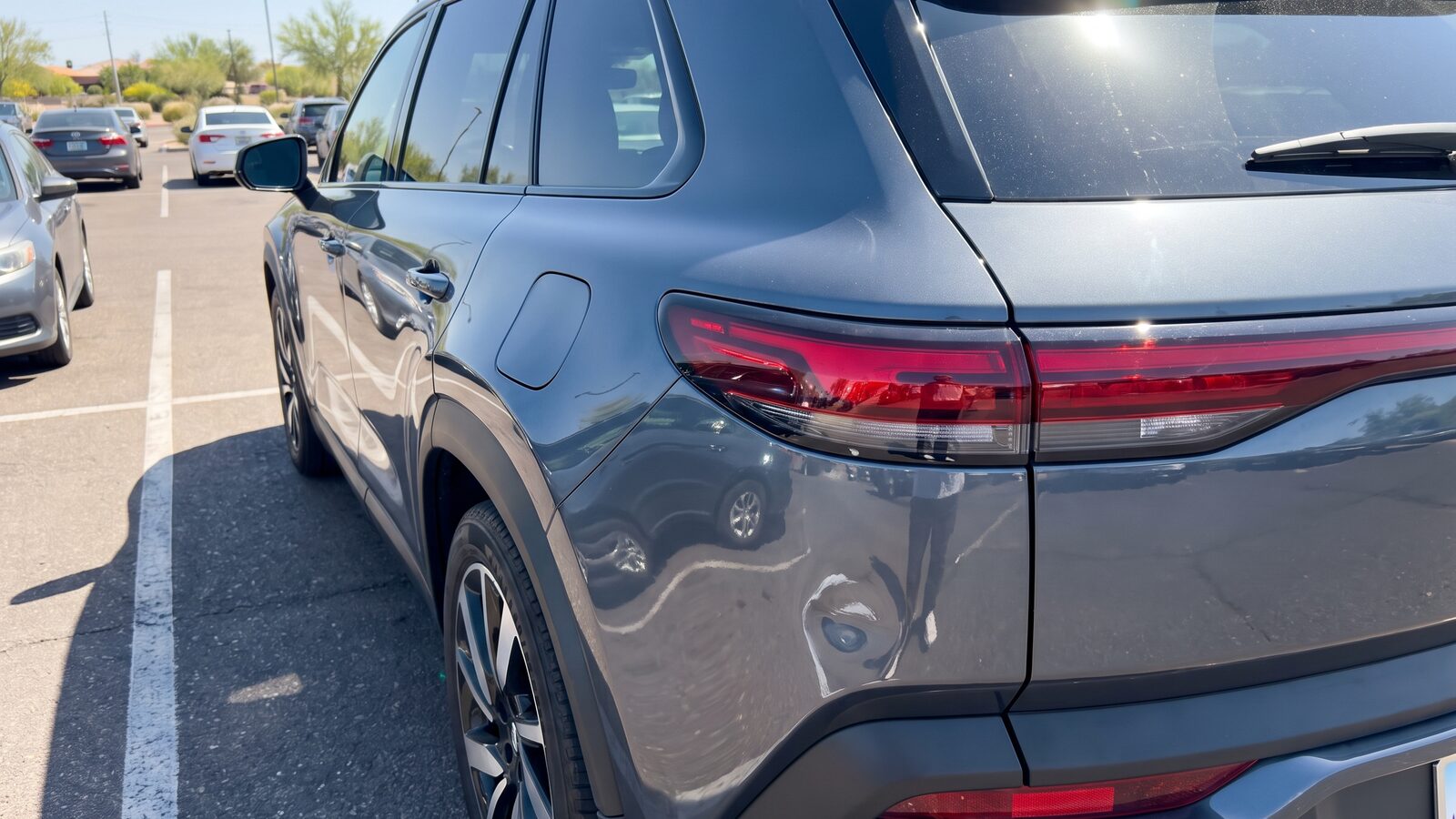 A small dent on the rear panel of a newer gray SUV in a sunny Phoenix parking lot